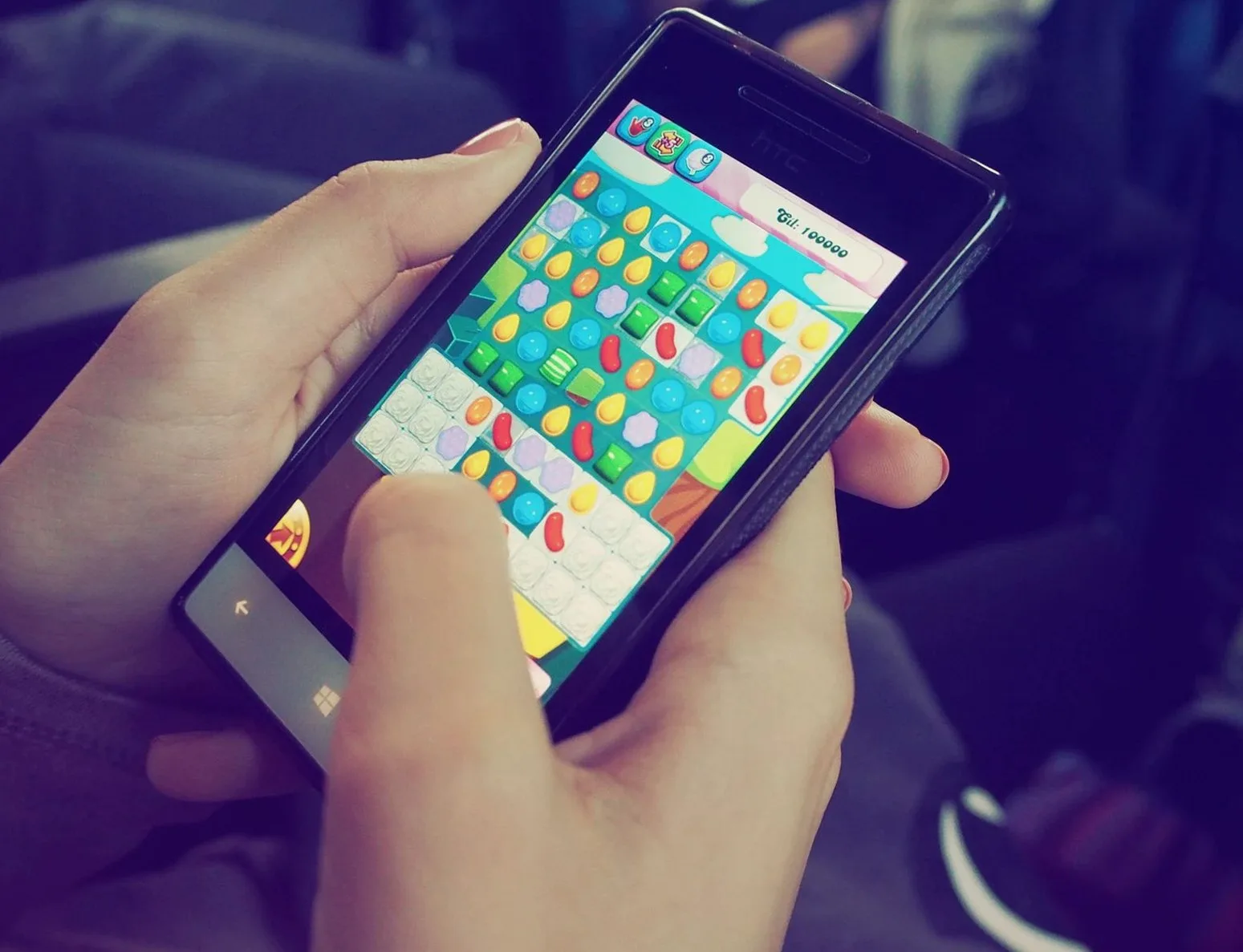 スマートフォンを両手で持ち、画面にカラフルなパズルゲームが表示されている様子。現代のテクノロジーを象徴している。