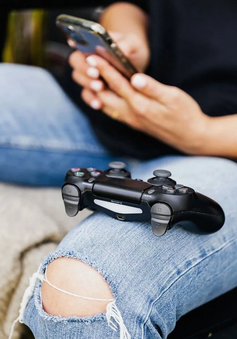 デニムパンツの上でスマートフォンとゲームコントローラーを持ちくつろぐ人物