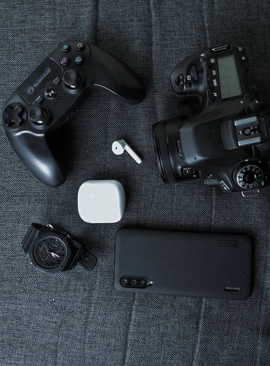 ゲームコントローラー、ワイヤレスイヤホン、カメラ、腕時計、スマートフォンが並ぶ平置きの写真