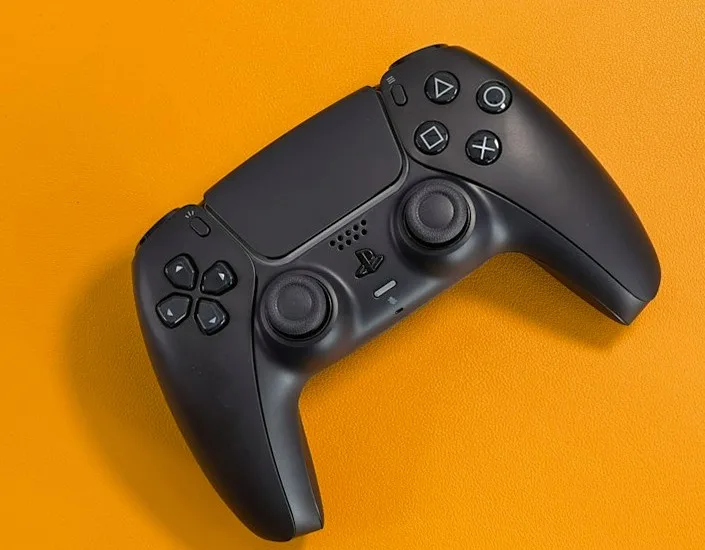 オレンジ色の背景に置かれた黒いPS5用ワイヤレスコントローラー